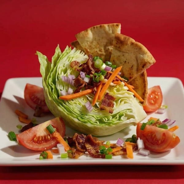 Wedge salad with bacon, tomatoes, carrots, onions, and pita bread on a white plate.