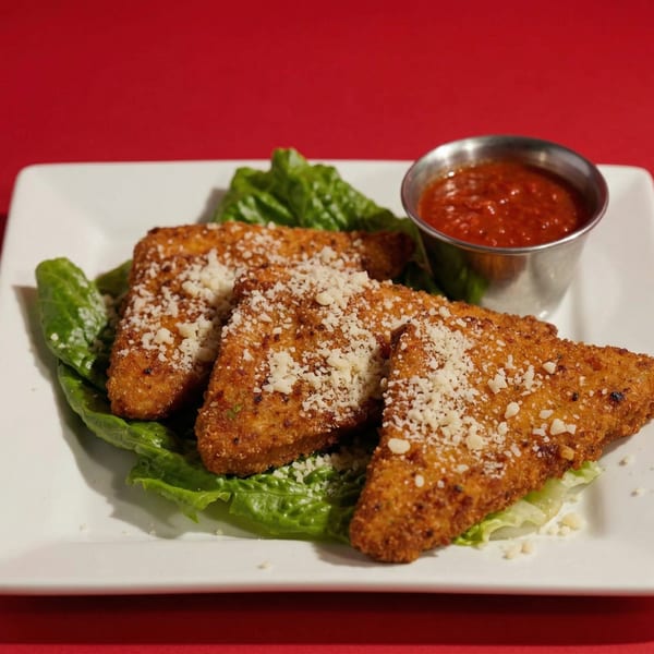 Three golden-brown fried mozzarella triangles topped with parmesan cheese, served with marinara sauce and lettuce.