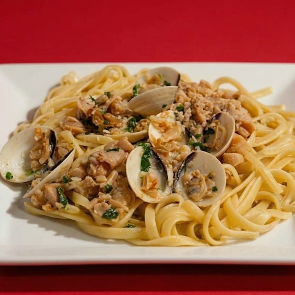 Linguine pasta with clams, chopped garlic, and parsley on a white rectangular plate.